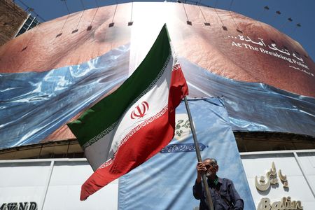 A man holds an Iranian flag near an anti-U.S. billboard
