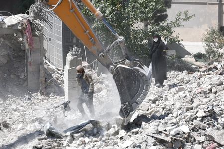 A woman stands among the rubble of her house, which