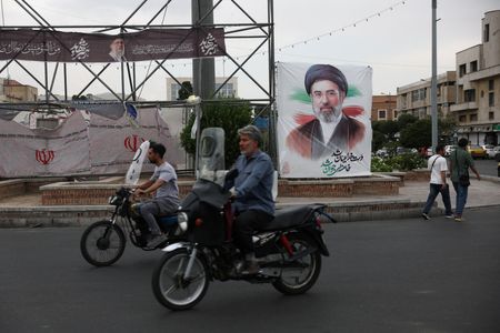People ride near a banner with an image of Iran's