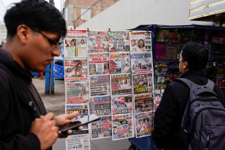 A man looks at a newspaper stand with headlines showing