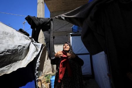 A displaced Palestinian woman hangs laundry at a shelter in