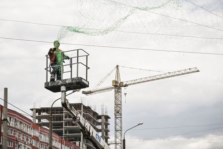 Municipal workers install anti-drone netting over a street on outskirts