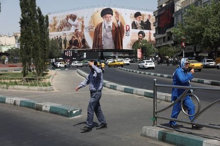 People walk past a billboard featuring images of Iran's late