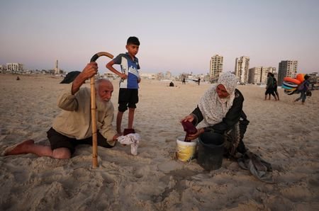 Displaced Palestinian woman washes clothes on the shore of the