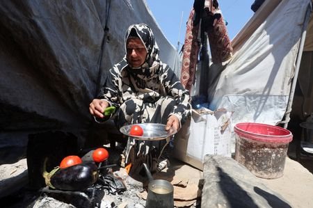 Displaced Palestinian woman Nisreen Abu Saada cook vegetables over a