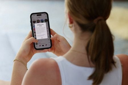 FILE PHOTO: A teenager poses holding a mobile phone displaying