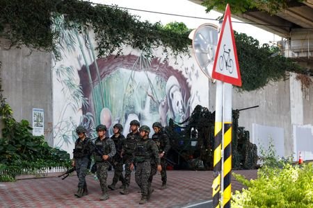 Soldiers walk past a camouflaged military vehicle during the annual