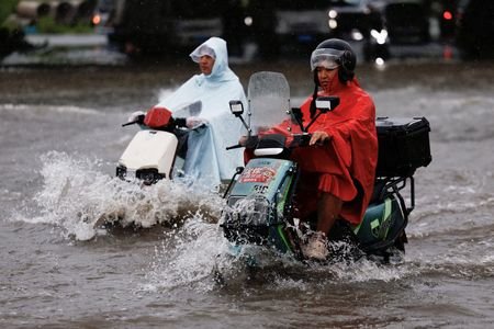 People ride on scooters as they travel through waters on