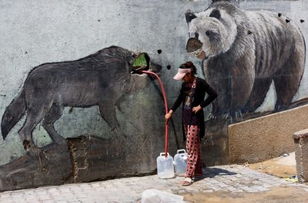 Palestinian girl fills water containers outside the wall of a
