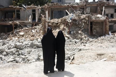 Iranian women look at a building, which was damaged in