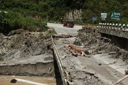 An auto rickshaw drives past a broken bridge following a