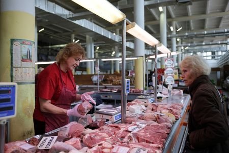 A vendor shows cuts of meat to a customer at