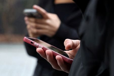 FILE PHOTO: Teenagers look at their mobile phone screens in