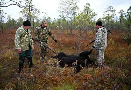 Hunters stand beside the carcass of a bear they shot