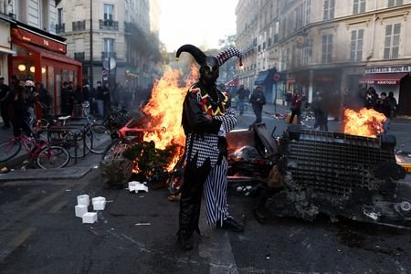 A demonstrator wearing a costume stands in front of burning